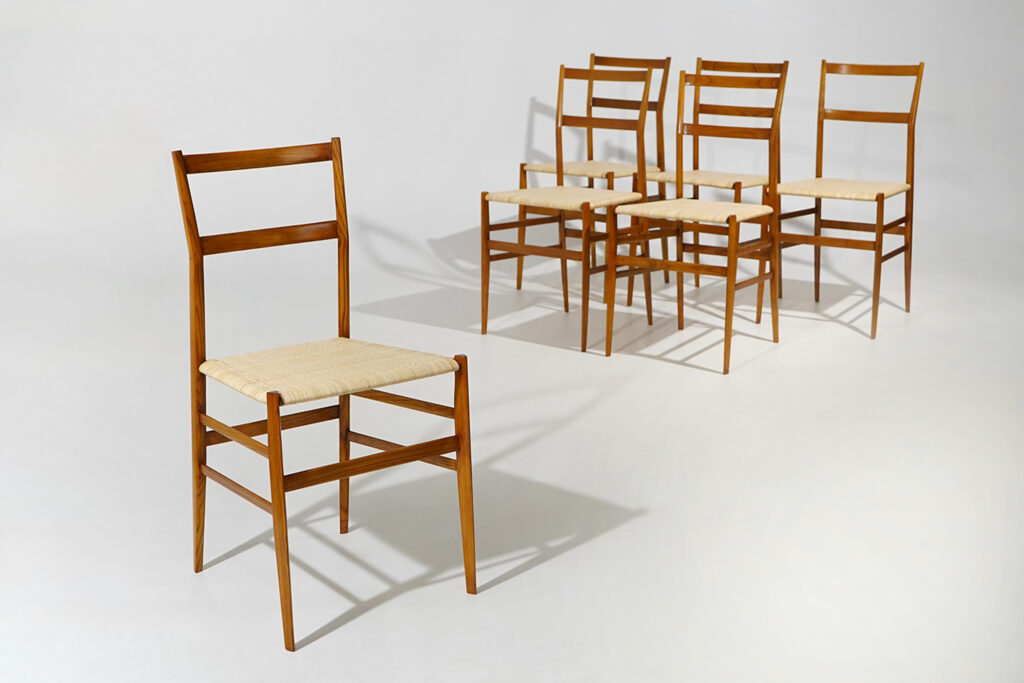 A set of six “Superleggera” dining chairs designed by Gio Ponti for Cassina in the 1950s, one of the most radical expressions of his pursuit of structural lightness. The design reduces the chair to a remarkably slender frame, balancing visual delicacy with a precise construction in which every element is reduced to what is strictly necessary. The narrow proportions, tapered legs and open backrest give the chair an almost graphic presence, while the woven seat introduces a tactile counterpoint to the rigorous wooden structure. The construction is defined by exceptionally fine sections and carefully resolved joints, with the legs tapering towards the floor and the back uprights continuing uninterrupted to frame two thin horizontal rails. The woven seat is stretched within the light wooden frame, reinforcing the contrast between structural economy and traditional craftsmanship. Despite its apparent fragility, the chair was conceived around a demanding relationship between minimum material and structural resistance, making lightness not simply an aesthetic quality but the central principle of the project. Cassina identifies the 699 Superleggera, introduced in 1957, as having an ashwood structure with legs of triangular section measuring only 18 mm. The Superleggera developed from Ponti’s long-standing interest in the traditional Chiavari chair, whose extreme economy of material and refined construction he reinterpreted through the language of modern industrial production. Rather than reproducing the historic type, Ponti progressively reduced and refined it until reaching an object in which craftsmanship and serial production became inseparable. This relationship with the Ligurian chair-making tradition is particularly significant in the present set, whose seats have been rewoven by craftsmen in Chiavari, reconnecting the restoration with the very tradition that informed the original design. Condition: Excellent overall condition. Provenance: Private residence, Cogoleto (GE). Restoration: Wooden elements refinished and polished. Seats rewoven by craftsmen in Chiavari. Documentation: Cassina advertisement, Domus, no. 330. Dimensions: Width 40 cm – Depth 45 cm – Height 82.5 cm – Seat height 45 cm